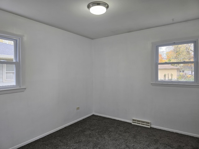 spare room featuring dark colored carpet, a healthy amount of sunlight, visible vents, and baseboards