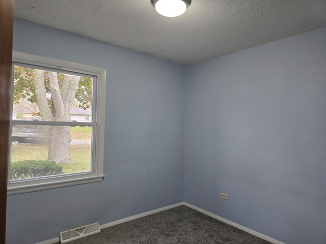 spare room featuring baseboards, visible vents, dark colored carpet, and a textured ceiling