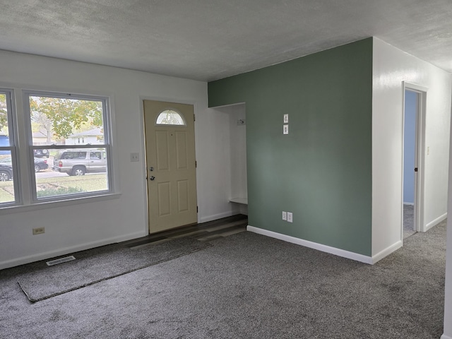 carpeted foyer entrance featuring visible vents, a textured ceiling, and baseboards