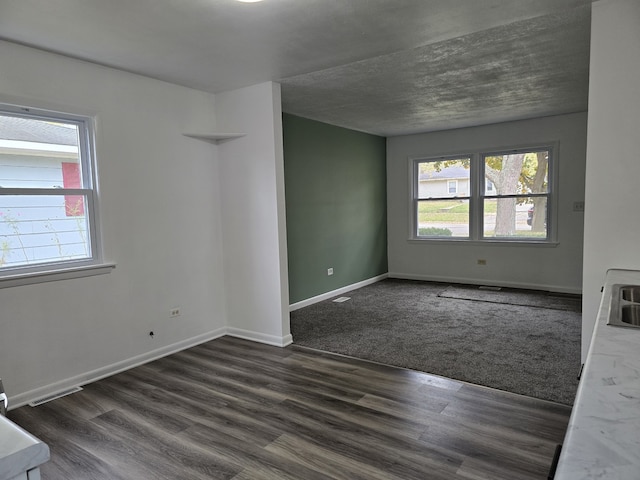 empty room featuring a wealth of natural light, dark wood finished floors, visible vents, and baseboards