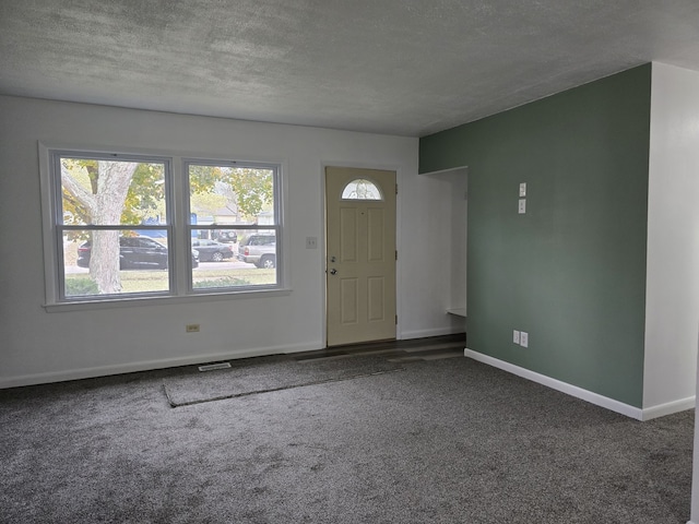 carpeted foyer with baseboards, a textured ceiling, visible vents, and a healthy amount of sunlight