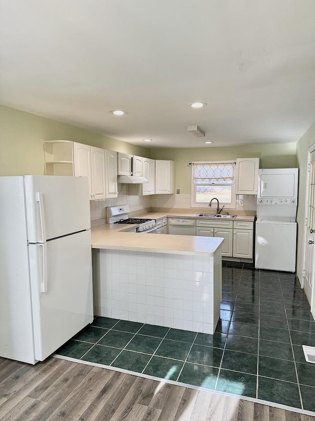 kitchen featuring tasteful backsplash, white cabinetry, a sink, stacked washing maching and dryer, and white appliances