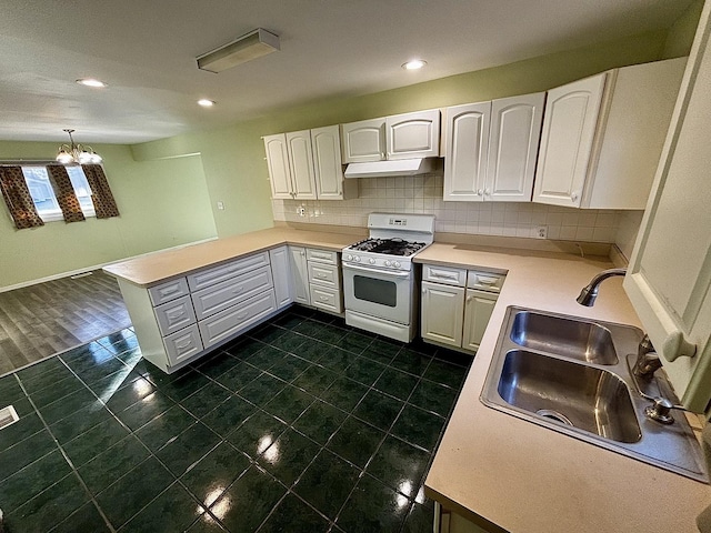 kitchen with white range with gas stovetop, a peninsula, a sink, white cabinets, and backsplash