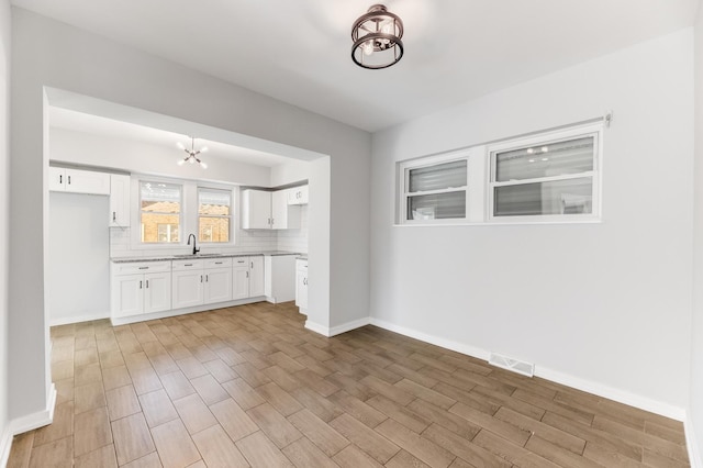 interior space featuring decorative backsplash, visible vents, white cabinetry, and a sink