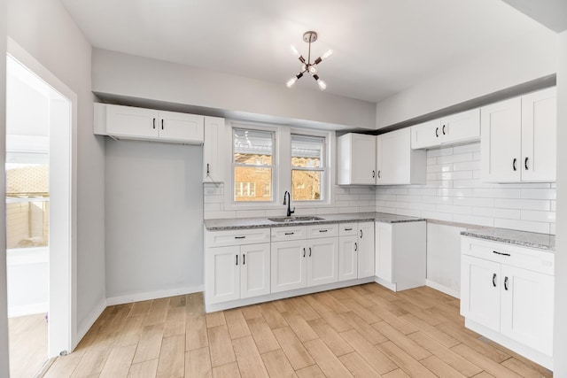 kitchen with tasteful backsplash, light stone countertops, light wood-style flooring, a notable chandelier, and a sink