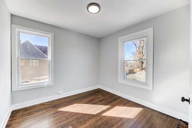 empty room featuring a wealth of natural light, dark wood-type flooring, and baseboards