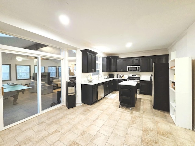 kitchen featuring a kitchen island, light countertops, dark cabinetry, stainless steel appliances, and open shelves