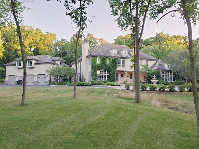 french country style house featuring a chimney, stucco siding, a front lawn, and a garage