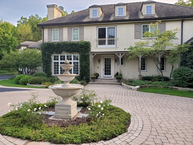view of front of home with stucco siding, a chimney, and curved driveway