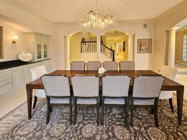 dining room featuring arched walkways, ornate columns, crown molding, a chandelier, and stairway