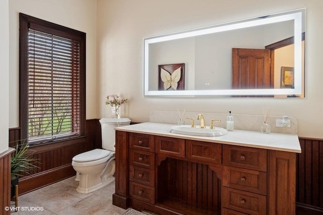 half bath featuring vanity, a wainscoted wall, and toilet