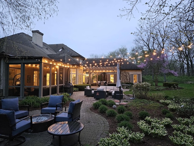 back of house with an outdoor living space with a fire pit, a patio, a pergola, a chimney, and a sunroom