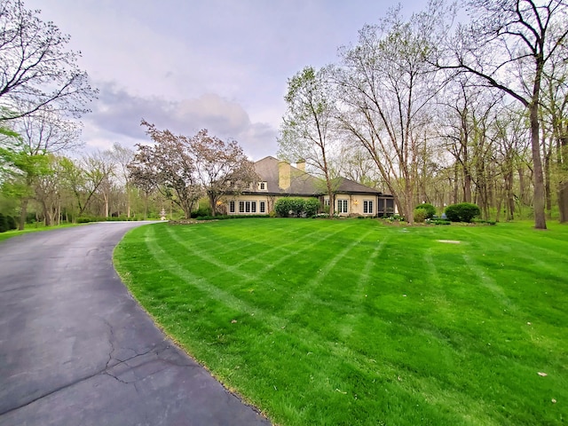 view of front of property featuring a front yard, a chimney, and asphalt driveway