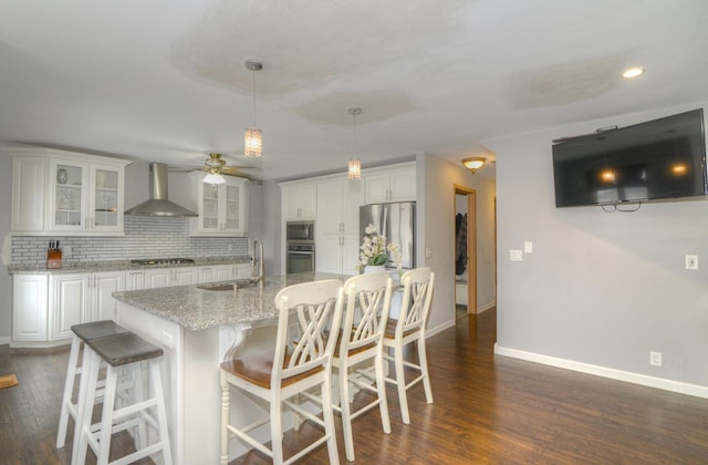 kitchen featuring a sink, white cabinets, appliances with stainless steel finishes, wall chimney exhaust hood, and backsplash