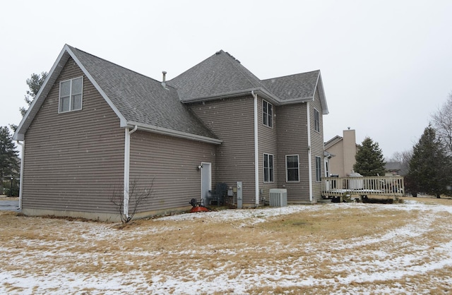 view of snow covered exterior with a wooden deck, cooling unit, and a shingled roof