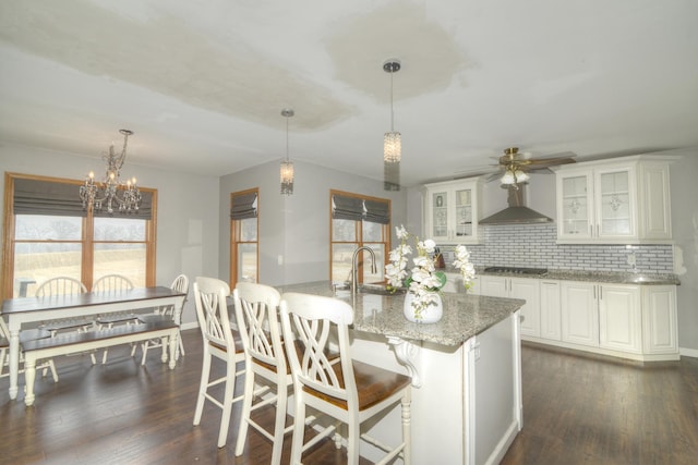 kitchen featuring decorative backsplash, light stone countertops, wall chimney exhaust hood, and dark wood-style flooring