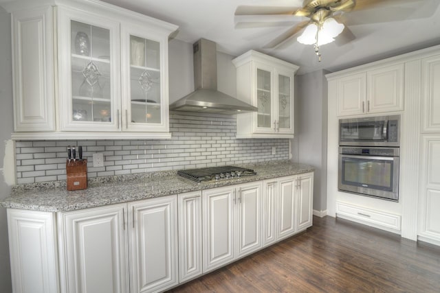 kitchen featuring backsplash, white cabinetry, stainless steel appliances, wall chimney range hood, and dark wood-style flooring