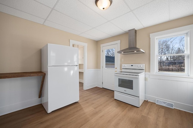 kitchen with visible vents, a drop ceiling, white appliances, light wood-style floors, and wall chimney exhaust hood