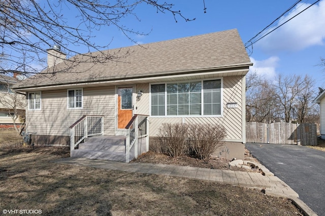 view of front of house featuring a shingled roof, a chimney, and fence