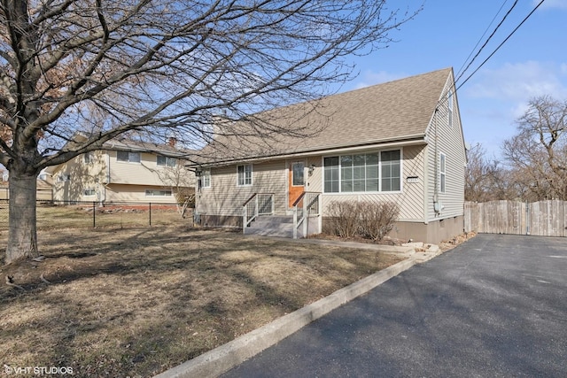 view of front facade featuring a shingled roof and fence