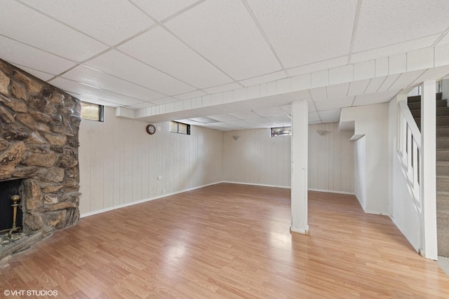 basement featuring a drop ceiling, light wood-type flooring, stairs, and a stone fireplace