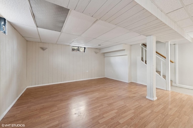 basement featuring a drop ceiling, baseboards, wood finished floors, and stairway