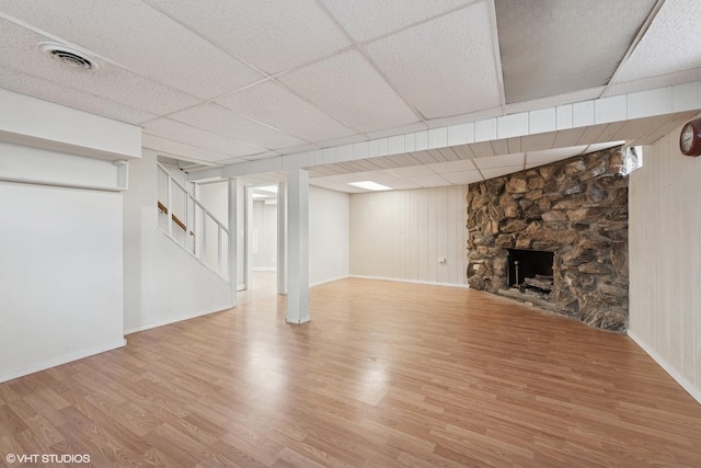 finished below grade area featuring wood finished floors, visible vents, a drop ceiling, a stone fireplace, and stairs