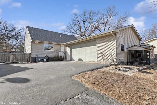 view of property exterior with aphalt driveway, cooling unit, fence, and a shingled roof