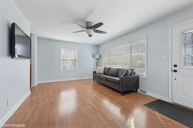 living room featuring visible vents, a ceiling fan, baseboards, and light wood finished floors