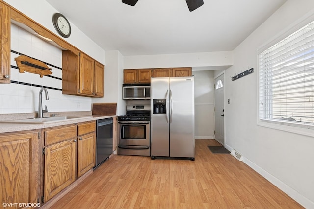 kitchen featuring brown cabinetry, light wood-style flooring, a sink, light countertops, and appliances with stainless steel finishes