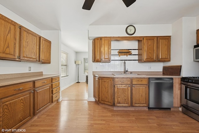 kitchen featuring backsplash, light wood-type flooring, brown cabinets, stainless steel appliances, and a sink