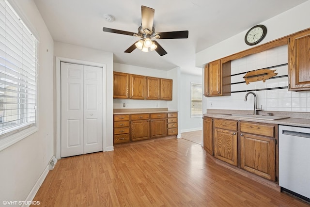 kitchen featuring stainless steel dishwasher, light wood-style flooring, brown cabinets, and a sink