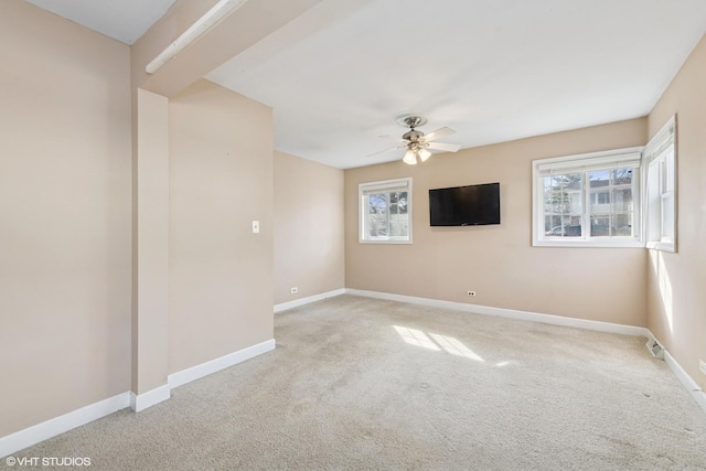 carpeted spare room with plenty of natural light, a ceiling fan, and baseboards