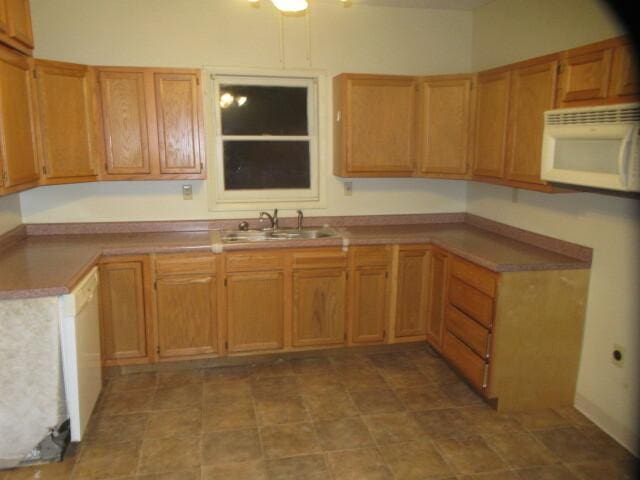 kitchen with brown cabinetry, white appliances, light countertops, and a sink