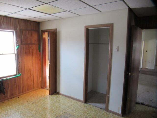 unfurnished bedroom featuring wood walls, multiple windows, and a drop ceiling