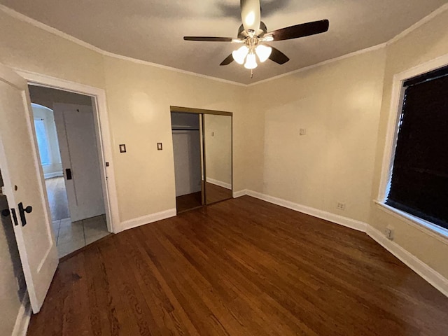 unfurnished bedroom with baseboards, a closet, wood finished floors, and crown molding