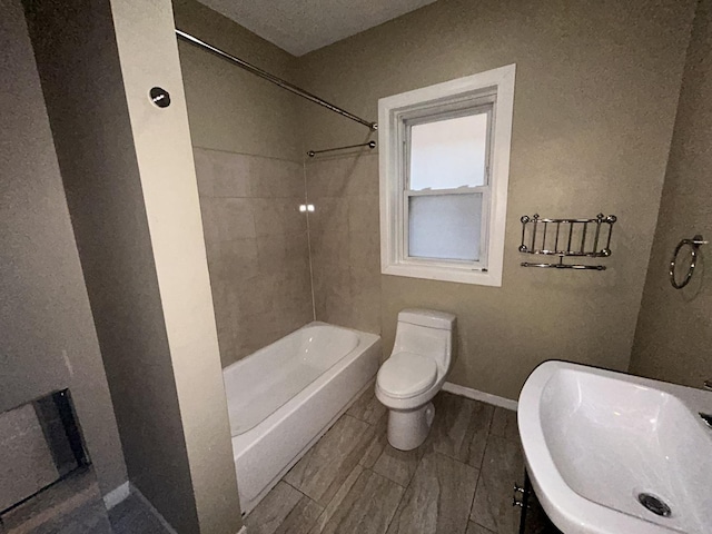 bathroom featuring tub / shower combination, a sink, toilet, and baseboards