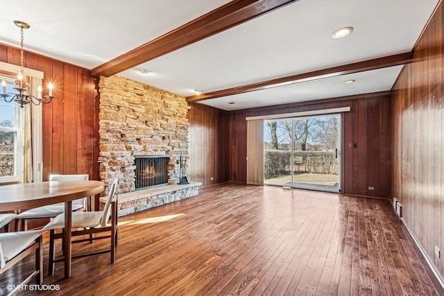 living area featuring a stone fireplace, beam ceiling, wood walls, and hardwood / wood-style floors