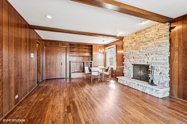 unfurnished living room with beam ceiling, wood-type flooring, wooden walls, an inviting chandelier, and a fireplace