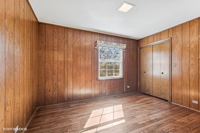 unfurnished bedroom with a closet, wooden walls, and wood finished floors