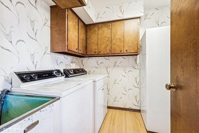 washroom featuring a sink, cabinet space, light wood-style floors, wallpapered walls, and washing machine and clothes dryer