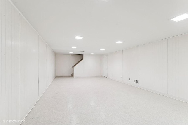 finished basement featuring visible vents, light floors, stairway, and a decorative wall