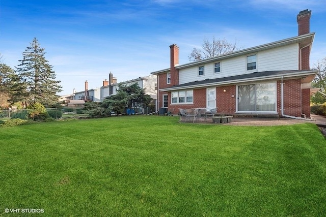 back of house featuring fence, a lawn, brick siding, and a chimney