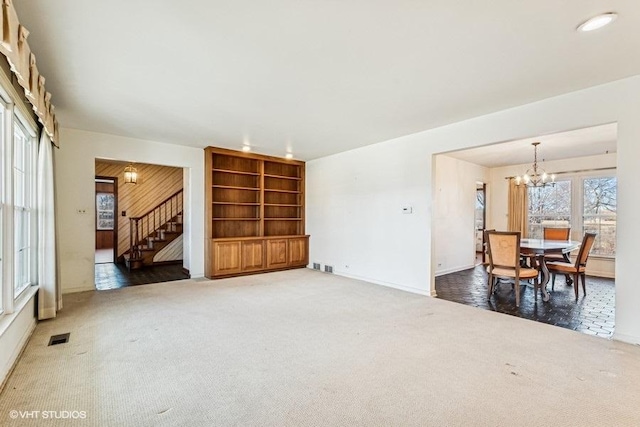 carpeted living area featuring visible vents, a chandelier, and stairs