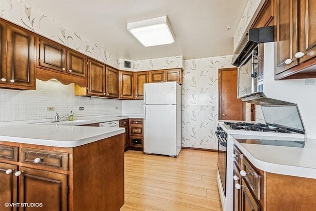 kitchen with freestanding refrigerator, light wood-style floors, wallpapered walls, gas range, and light countertops