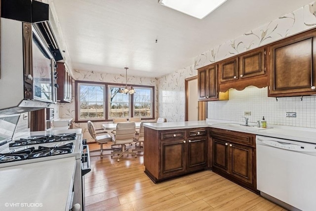 kitchen featuring wallpapered walls, light countertops, a peninsula, white dishwasher, and a sink