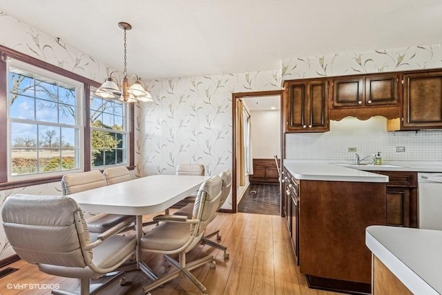 kitchen featuring wallpapered walls, dishwasher, light countertops, light wood-style flooring, and a notable chandelier