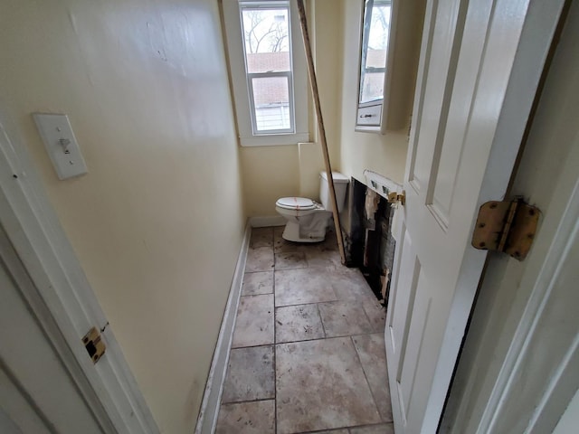 bathroom featuring stone tile flooring, baseboards, and toilet