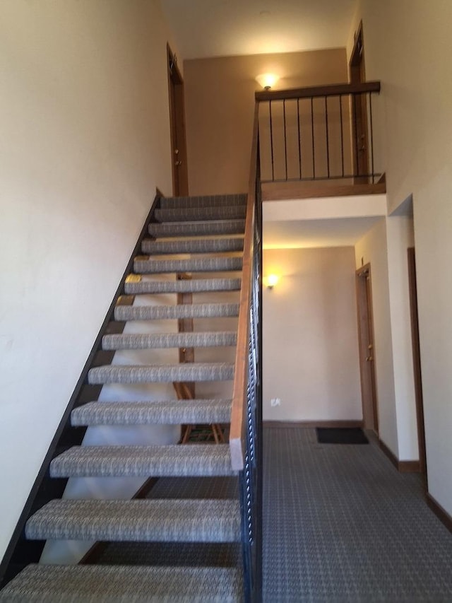 staircase featuring baseboards, carpet, and a towering ceiling