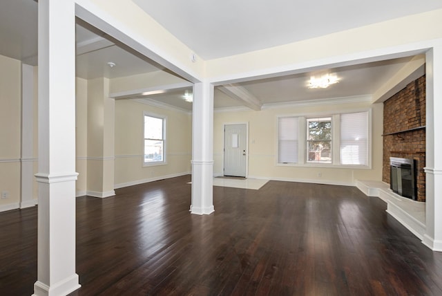 unfurnished living room featuring a fireplace, wood finished floors, and ornate columns